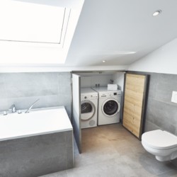Modernes Bad im Luxus Penthouse in Bad Wiessee mit Badewanne, Dachfenster und Waschmaschinen.