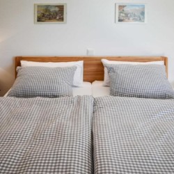 Gemütliches Schlafzimmer in Schliersee-Spitzingsee Ferienwohnung mit karierten Bettbezügen, Holzkopfteil und stimmungsvoller Beleuchtung.