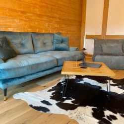 Gemütliches Wohnzimmer in einer Ferienwohnung in Schliersee mit Holzverkleidung, stilvollem Sofa und Kuhfellteppich.