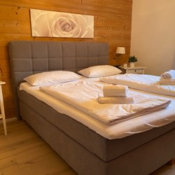 Gemütliches Schlafzimmer in Schlierseer Ferienwohnung "Taubenstein" mit Doppelbett, Holzwand & Kunst. Ideal für Erholung.
