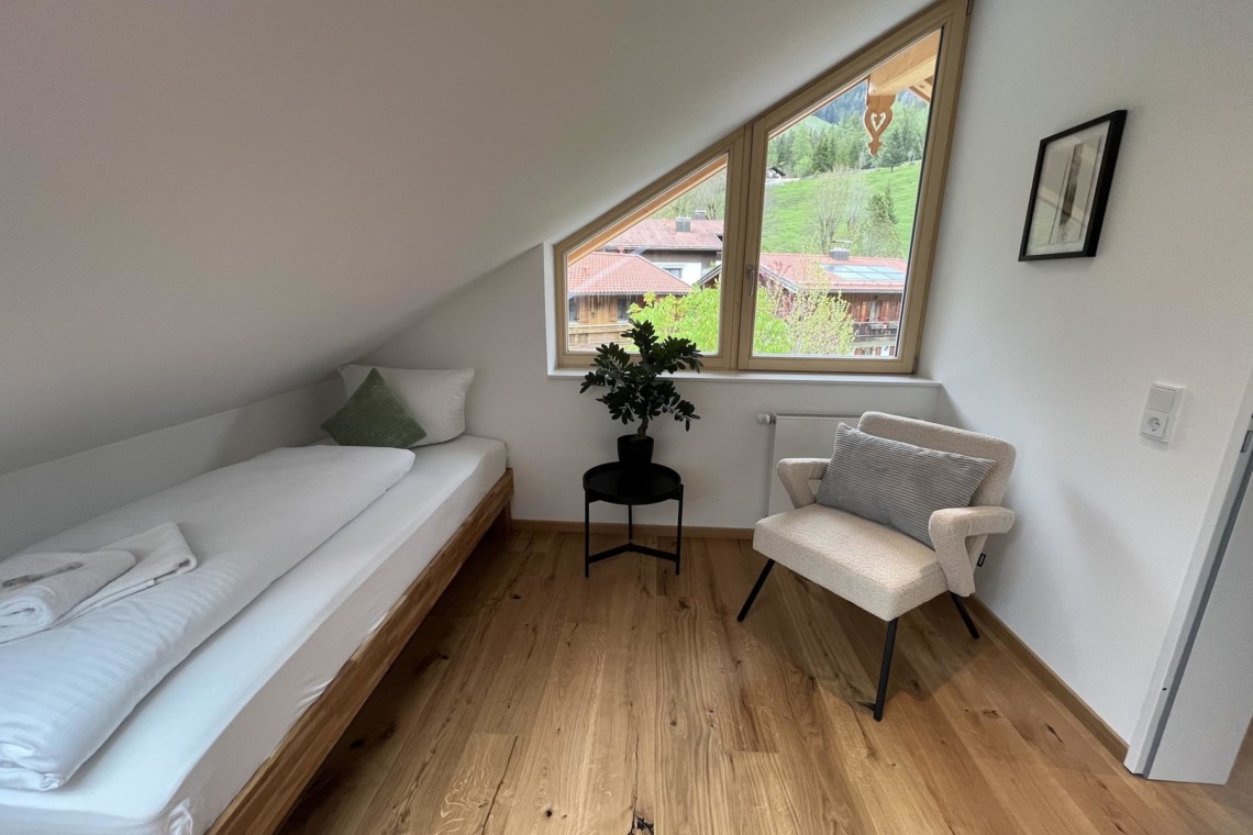 Gemütliches Zimmer in Bayrischzell Ferienwohnung mit Holzboden, Sofa, Pflanze und Bergblick.