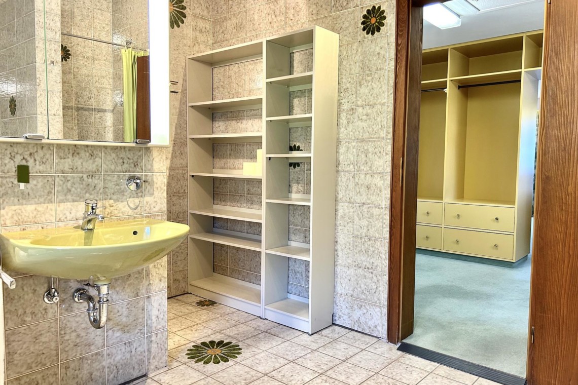 Helles Badezimmer in Schliersee Ferienwohnung mit Spiegel, Regal und bequemen Zugang zum Ankleidezimmer.