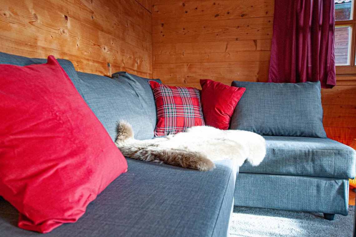 Gemütliche Ferienwohnung-Ecke in Schliersee mit Sofa, Kissen und Holzwand für einen erholsamen Urlaub.