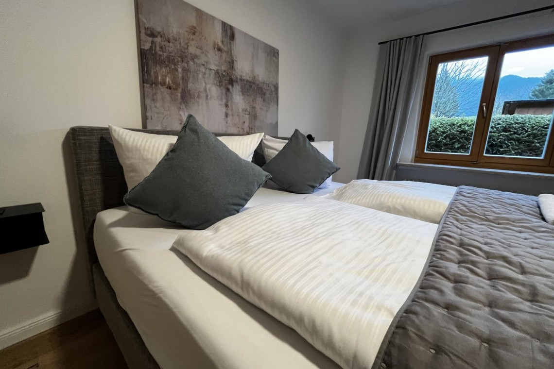 Gemütliches Zimmer mit Doppelbett, stilvollem Wandbild und Fensterblick in Rottach-Egern. Ideal für eine entspannte Auszeit.