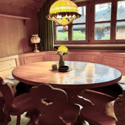 Gemütliche Ferienwohnung am Tegernsee: holzgetäfeltes Interieur, runder Tisch, helle Lampe, authentisches Alpenflair in Rottach-Egern.