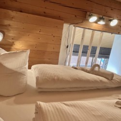 Gemütliches Schlafzimmer mit Holzvertäfelung, weiße Bettwäsche und Zugang zum Balkon in Schliersee Ferienwohnung.