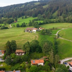 Luftaufnahme von Fischbachau: Grüne Wiesen, Ferienwohnungen umgeben von Wäldern, idyllische Natur. Ideal für Erholung.