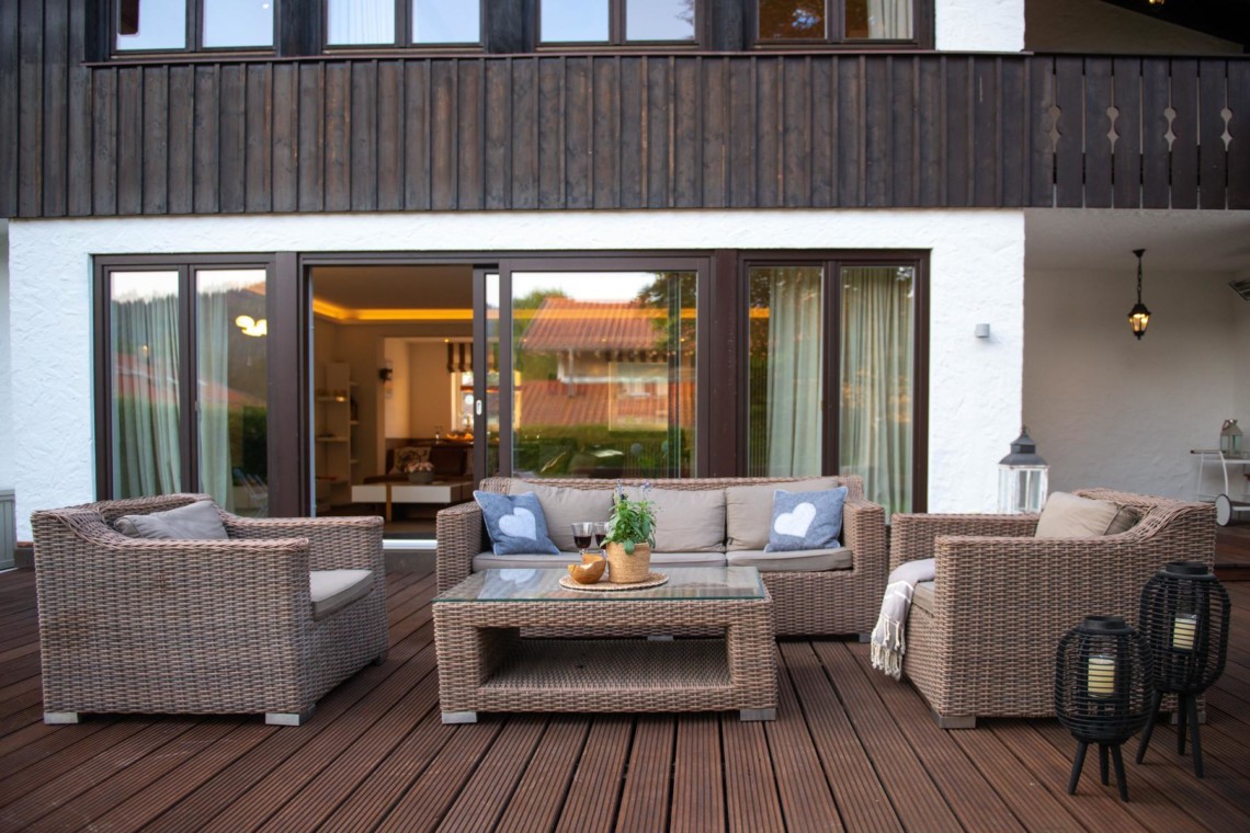 Gemütliche Terrasse eines Ferienhauses in Schliersee mit Lounge-Möbeln und Blick ins Innere.