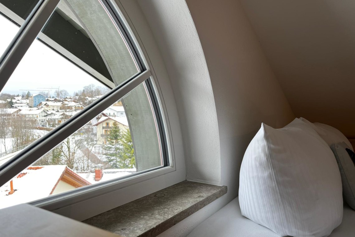 Gemütliche Eckcouch mit Blick aus Dachfenster auf verschneites Gmund am Tegernsee – ideal für Urlaub.