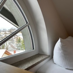 Gemütliche Eckcouch mit Blick aus Dachfenster auf verschneites Gmund am Tegernsee – ideal für Urlaub.