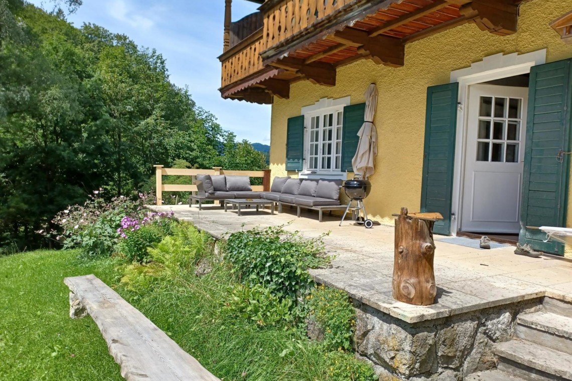 Gemütliche Terrasse einer Ferienwohnung in Geitau mit Sofa und grüner Umgebung.