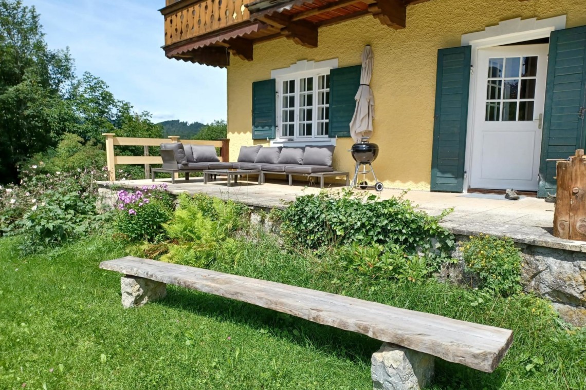 Gemütliche Terrasse einer Ferienwohnung in Geitau mit Holzmöbeln und grüner Umgebung.