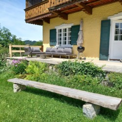 Gemütliche Terrasse einer Ferienwohnung in Geitau mit Holzmöbeln und grüner Umgebung.