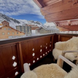 Gemütlicher Balkon einer Ferienwohnung mit Aussicht auf die schneebedeckten Berge von Warth am Arlberg.