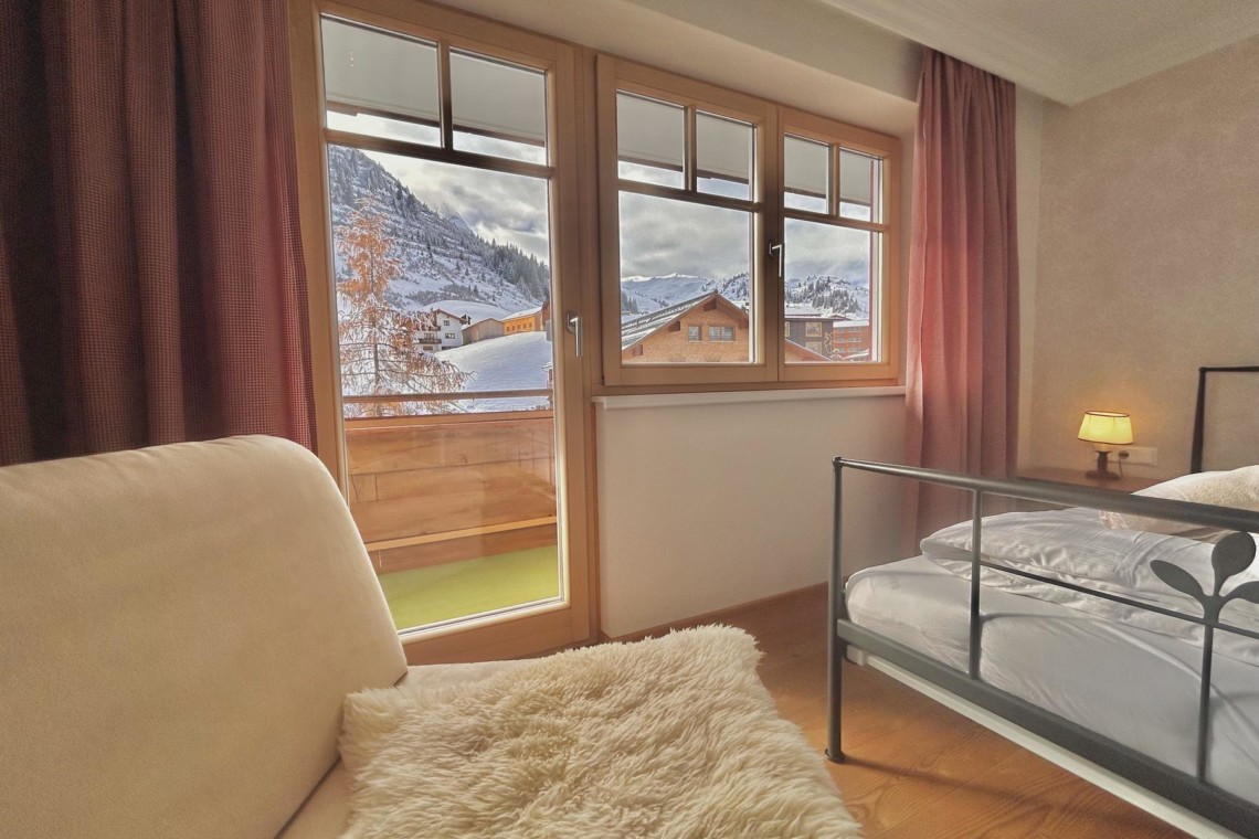Gemütliches Schlafzimmer mit einem tollen Blick auf die verschneiten Berge von Warth am Arlberg. Ideal für Urlaub!