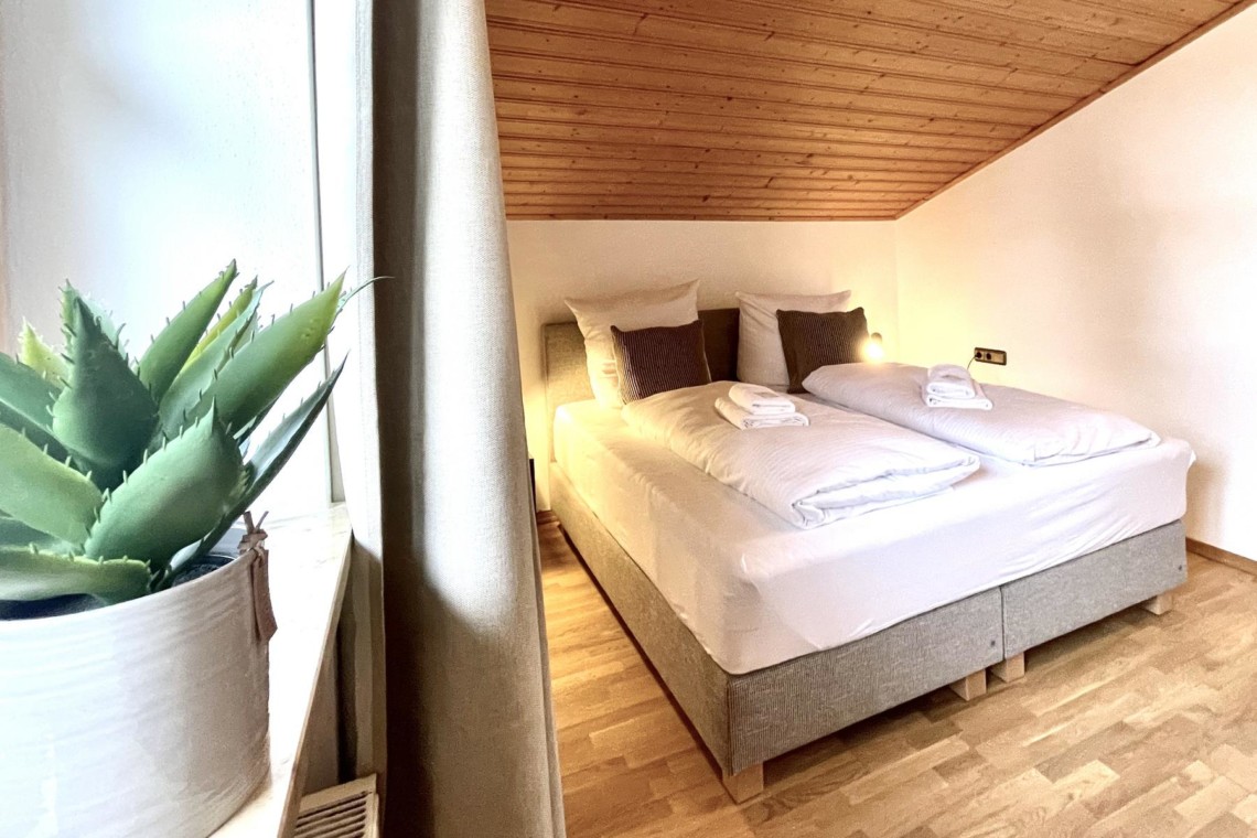 Gemütliches Schlafzimmer in Ferienwohnung am Tegernsee mit Doppelbett und Holzdecke. Ideal für Urlaub in Rottach-Egern.