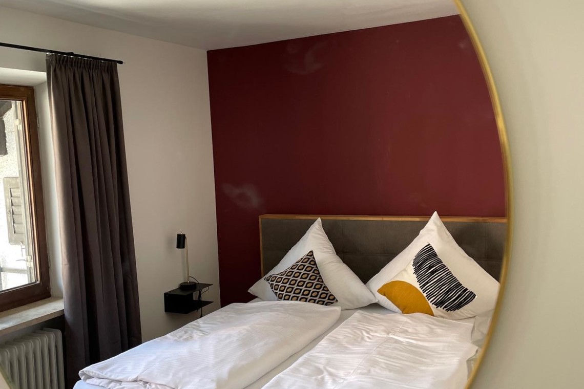 Gemütliches Schlafzimmer in Tegernseer Ferienwohnung, stilvoll mit rot akzentuierter Wand.