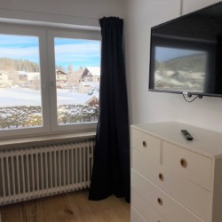 Gemütlicher Ferienwohnungsraum in Bad Wiessee mit Blick auf Schnee, TV und Kommode.