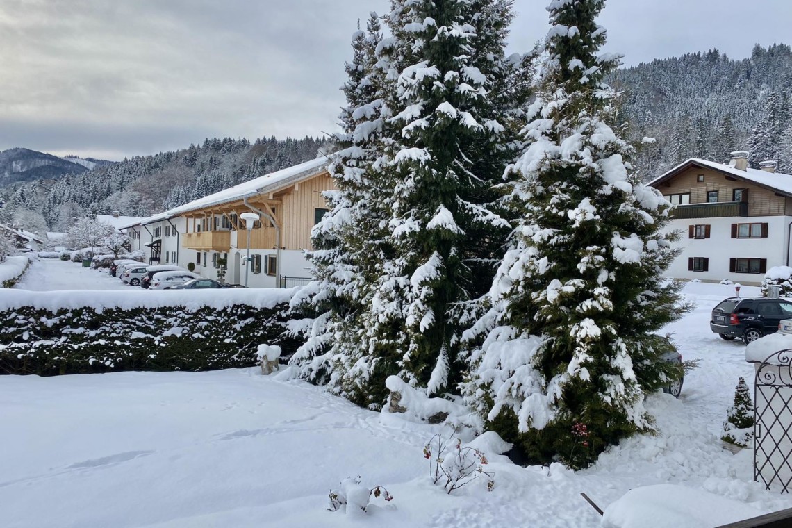 Gemütliche Winteransicht einer Ferienunterkunft in Bad Wiessee mit verschneiten Bäumen und Alpenpanorama.