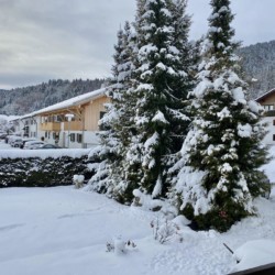 Gemütliche Winteransicht einer Ferienunterkunft in Bad Wiessee mit verschneiten Bäumen und Alpenpanorama.
