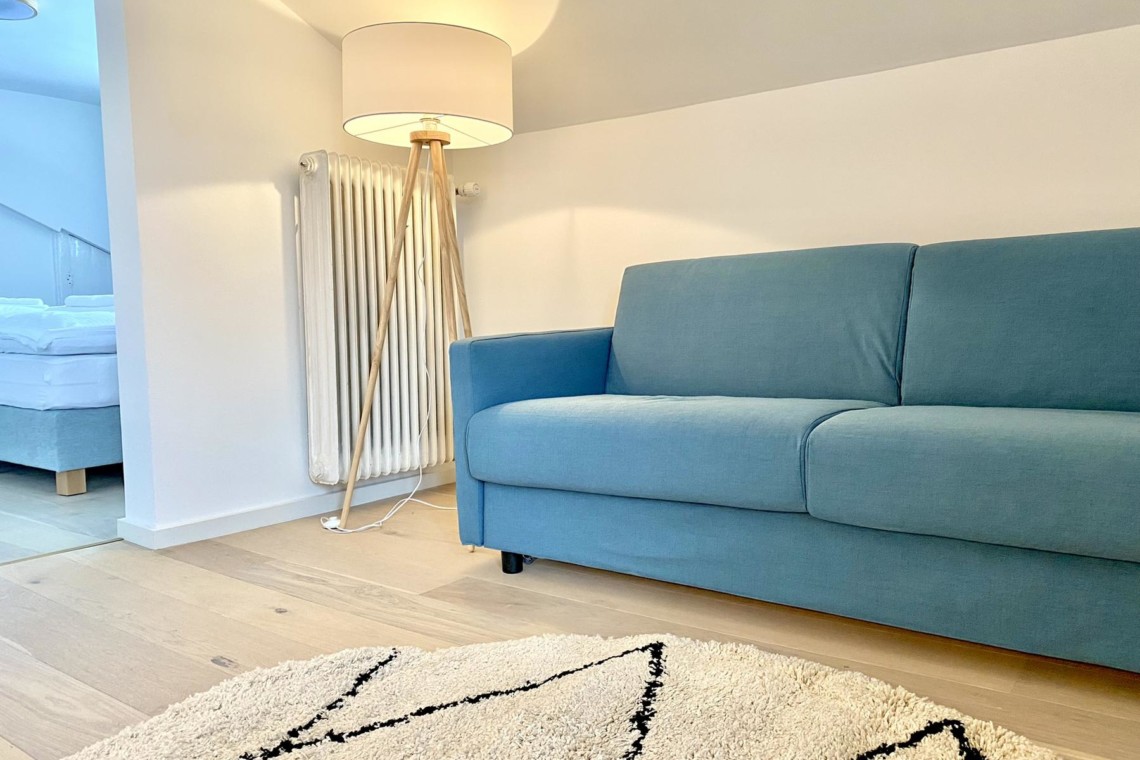 Helle FeWo in Bad Wiessee mit blauem Sofa, modernem Ambiente & gemütlicher Atmosphäre. Ideal für Erholungssuchende.