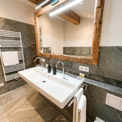 Modernes Badezimmer in Kreuth Ferienwohnung mit Holzelementen und Natursteintiles. Ideal für eine entspannende Auszeit. #KreuthUrlaub