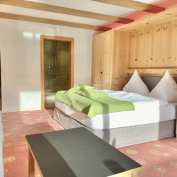 Gemütliches Zimmer in Bad Wiessee mit Bett, Holzmöbeln und Dusche. Ideal für den Urlaub am Tegernsee.