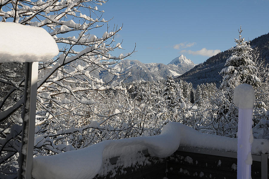 Idyllischer Winterblick vom Balkon eines Ferienhauses in Schliersee-Neuhaus, umgeben von schneebedeckten Bäumen und Bergen.