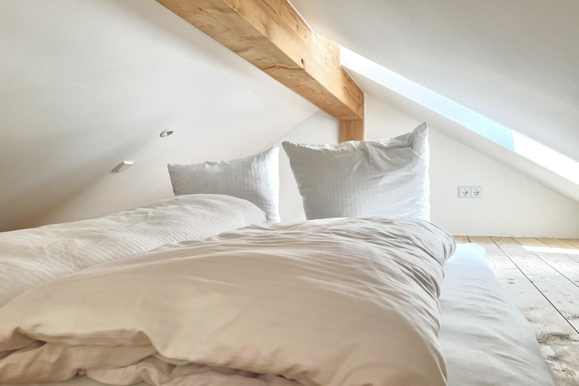 Gemütliches Dachzimmer mit Holzbalken und weicher Bettwäsche in Bayrischzell – ideal für Urlaub in den Bergen!