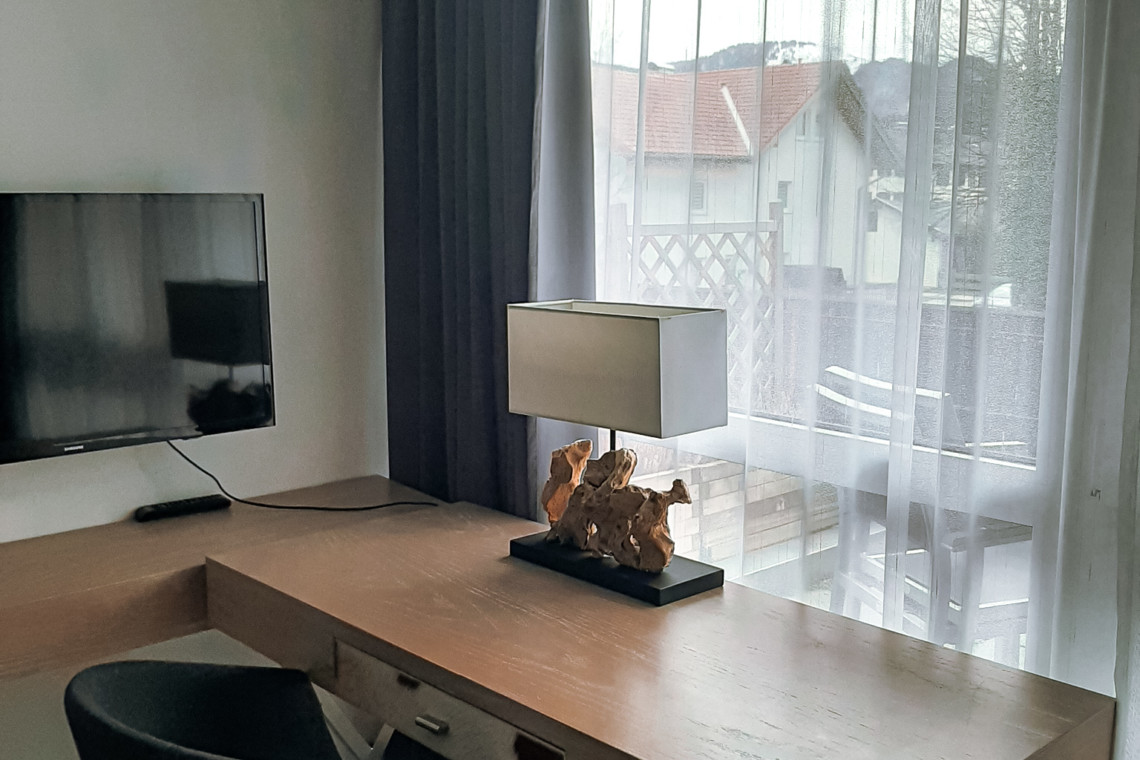 Gemütliches Wohnzimmer mit modernem TV, Schreibtisch und Balkontür mit Blick auf die Berge von Schliersee. Ideal für Entspannung.