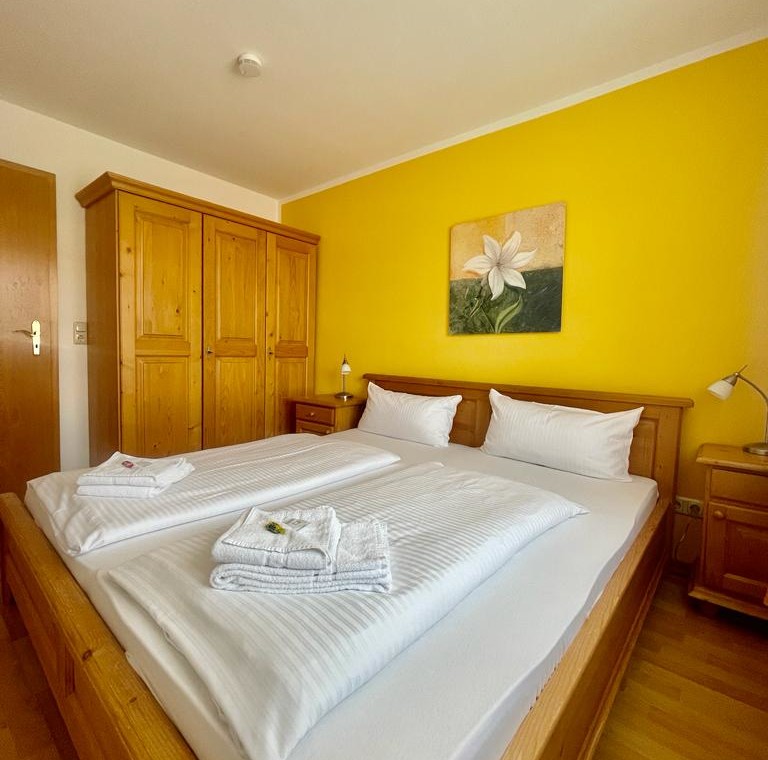 Gemütliches Schlafzimmer in Bad Wiesseer Ferienwohnung mit gelben Wänden und Holzmöbeln.