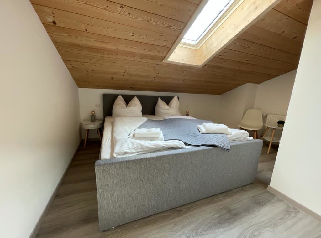 Gemütliches Dachzimmer in Bad Wiessee Ferienwohnung mit Doppelbett, Holzdecke und hellem Interieur.