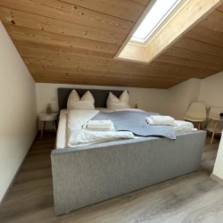 Gemütliches Dachzimmer in Bad Wiessee Ferienwohnung mit Doppelbett, Holzdecke und hellem Interieur.