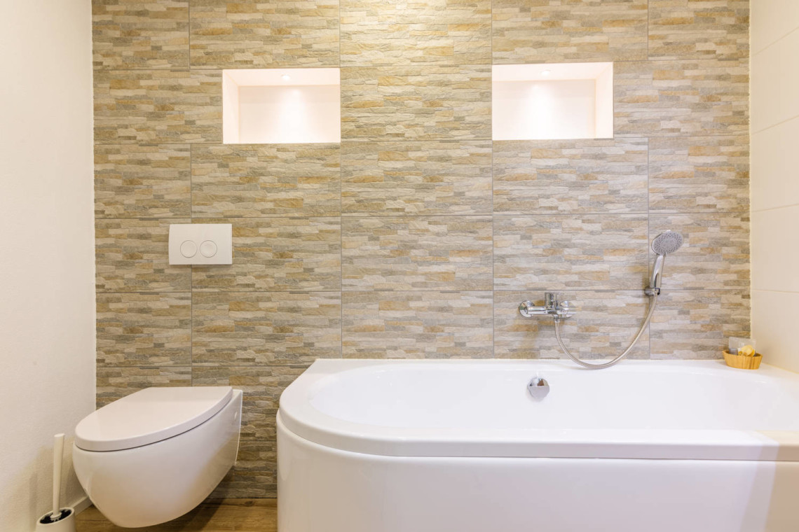 Modernes Badezimmer in einer Ferienwohnung in Schliersee mit eleganter Badewanne und Steinwand.
