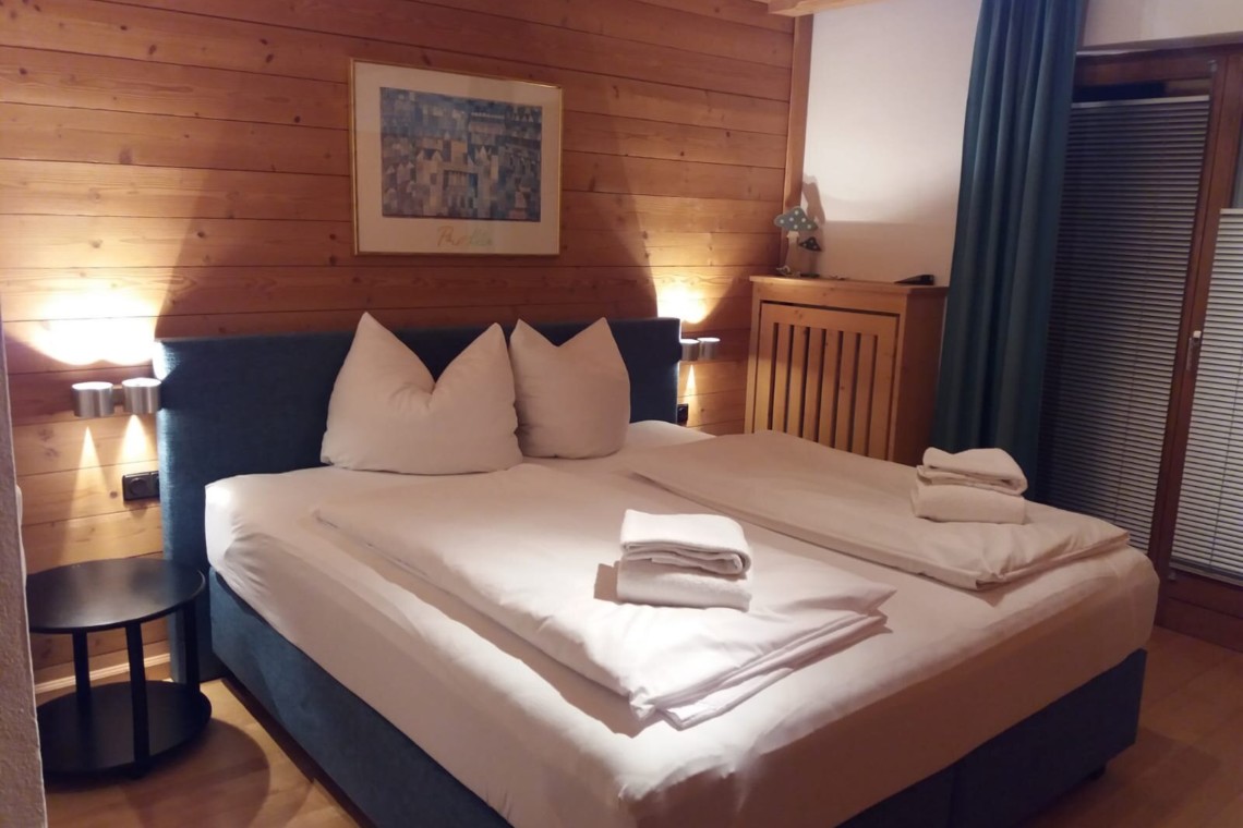 Gemütliches Schlafzimmer in Ferienwohnung Alpensonne, Schliersee, mit Holzwänden, Doppelbett und angenehmer Beleuchtung.