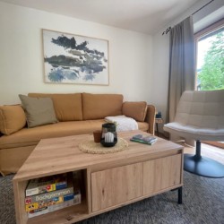Gemütliches Wohnzimmer in Ferienwohnung am Schliersee mit Sofa, Kunst an der Wand und Naturblick.