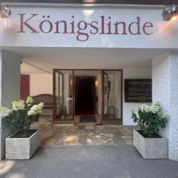 Eingangsbereich der "Königslinde" Ferienwohnung in Thiersee mit Pflanzen und Schild, einladende und ruhige Atmosphäre.