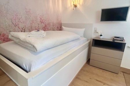 Gemütliches Schlafzimmer in Ferienwohnung mit Doppelbett, TV und stilvoller Dekoration. Ideal für erholsamen Urlaub.